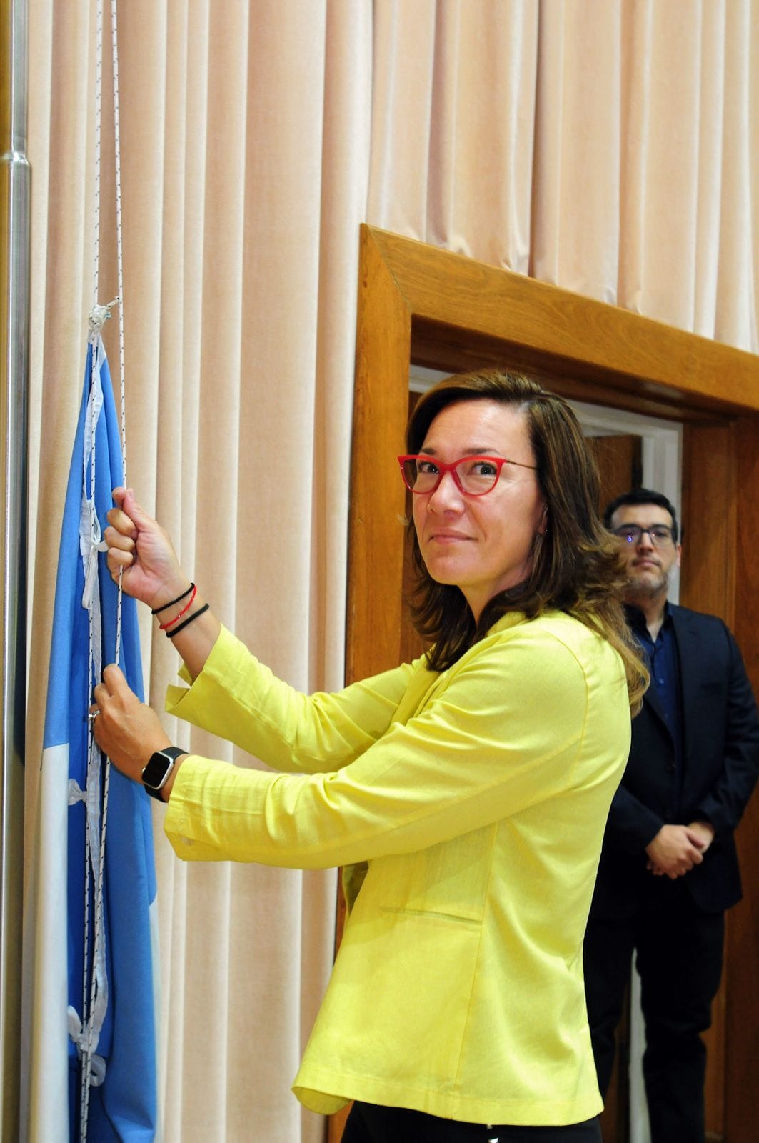 Izamiento de la bandera argentina durante un acto institucional en un salón oficial.