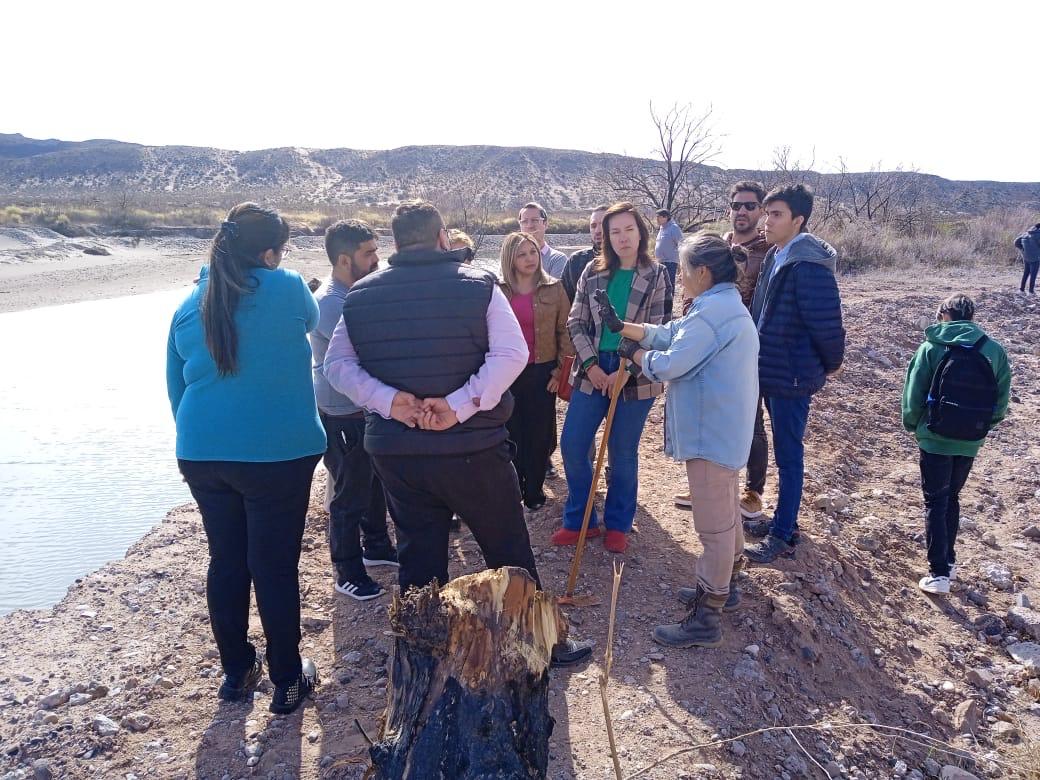 Grupo de vecinos y vecinas escucha una explicación durante una recorrida a orillas de un río.
