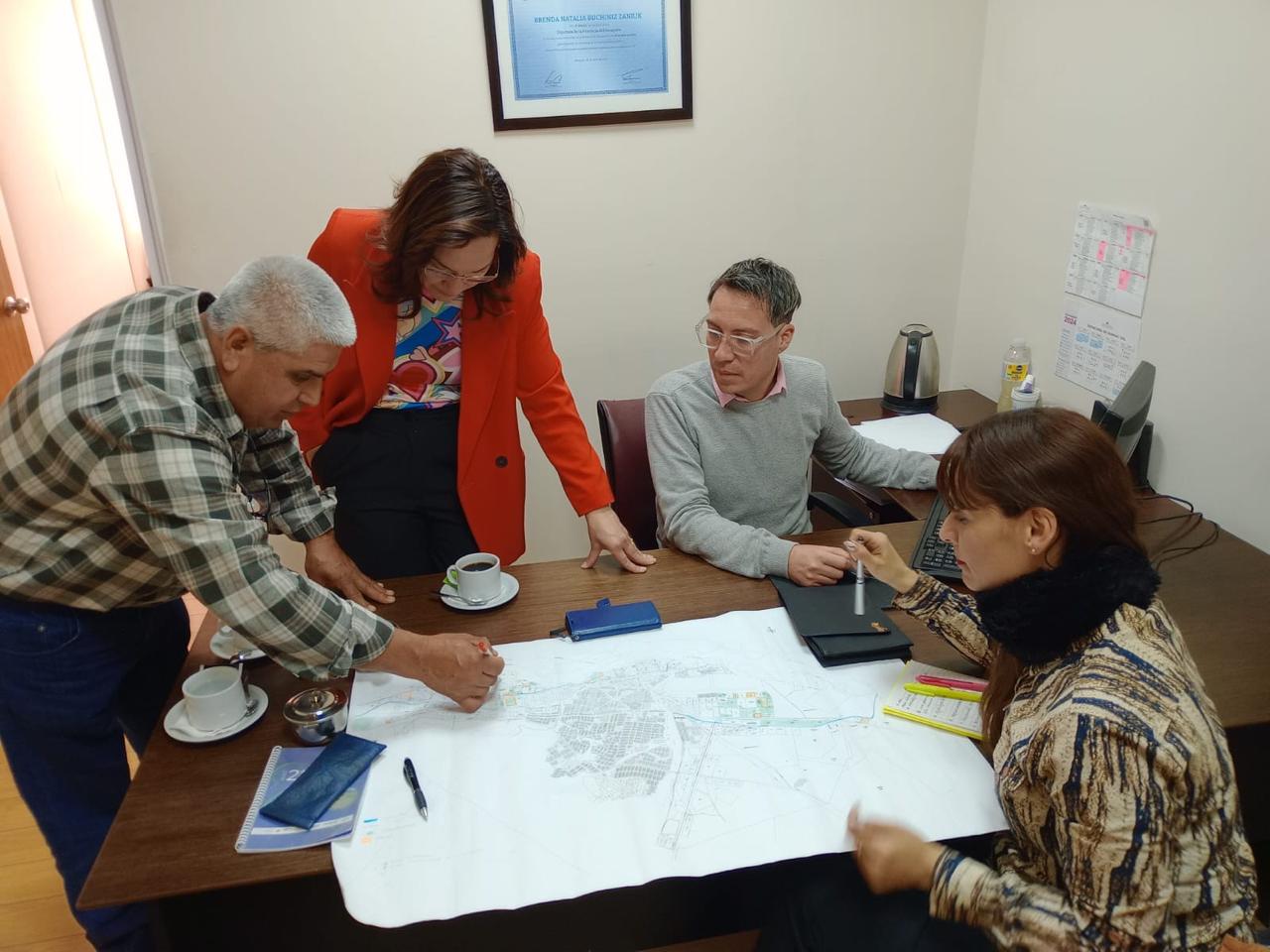 Reunión de trabajo en una oficina alrededor de un plano urbano desplegado sobre la mesa.